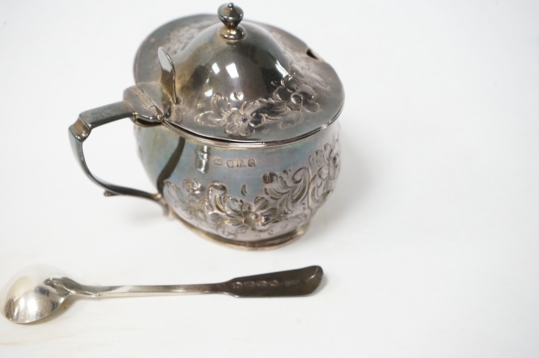 A George III silver oval mustard pot, with later embossed decoration, London, 1810, together with an associated silver mustard ladle. Condition - fair